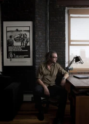 Man in olive shirt and glasses seated at a wooden desk in an interior styled by Megan Morton.