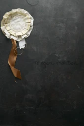 Cream and white fabric award rosette with a long brown ribbon on a dark textured background