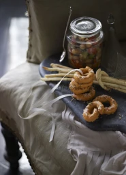 Stacked ring-shaped savory pastries and breadsticks on a dark platter with a glass jar of vegetables, styled by Megan Morton.