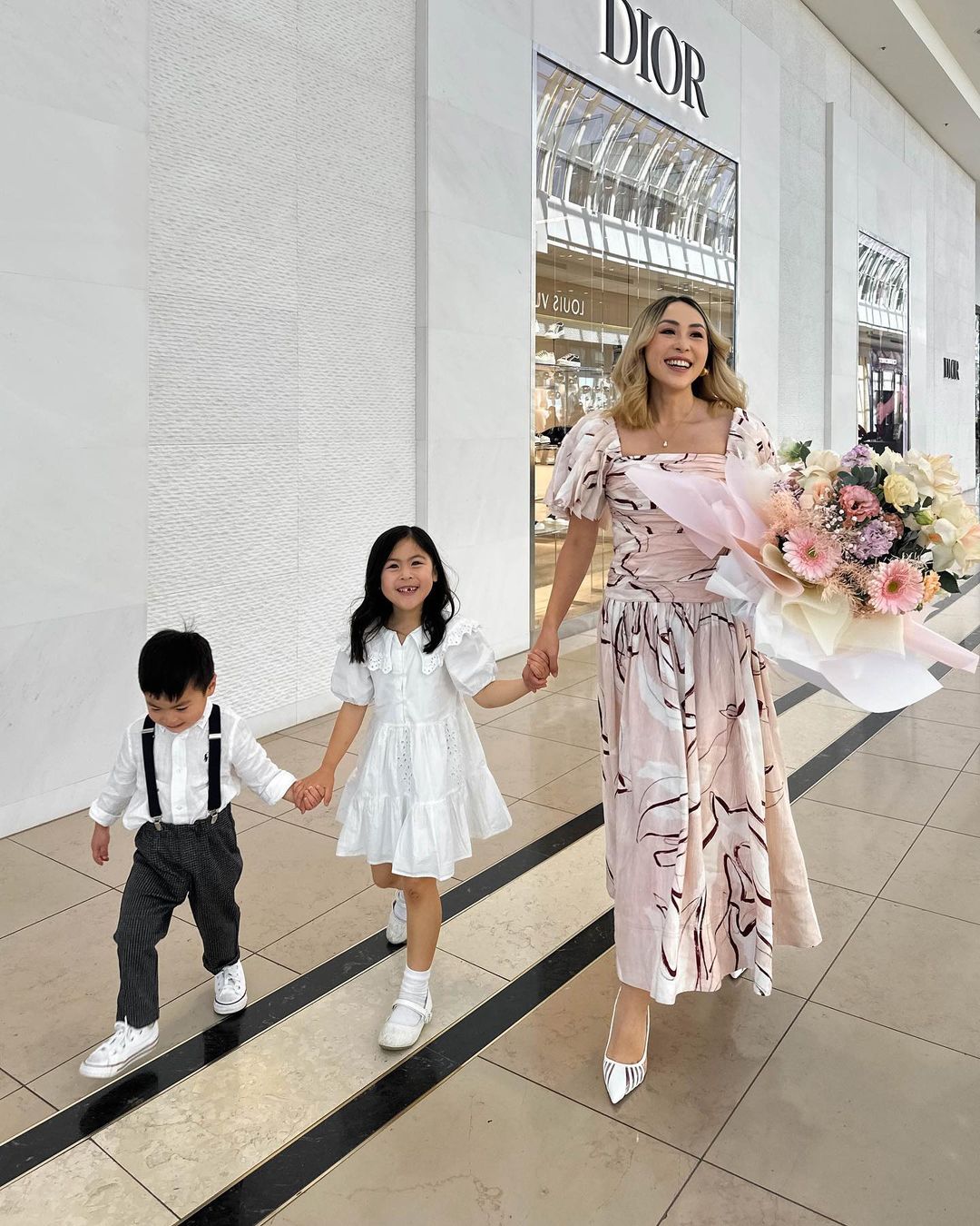 Stylish mother and two children walking out of a DIOR store with a large flower bouquet, capturing a lifestyle moment.