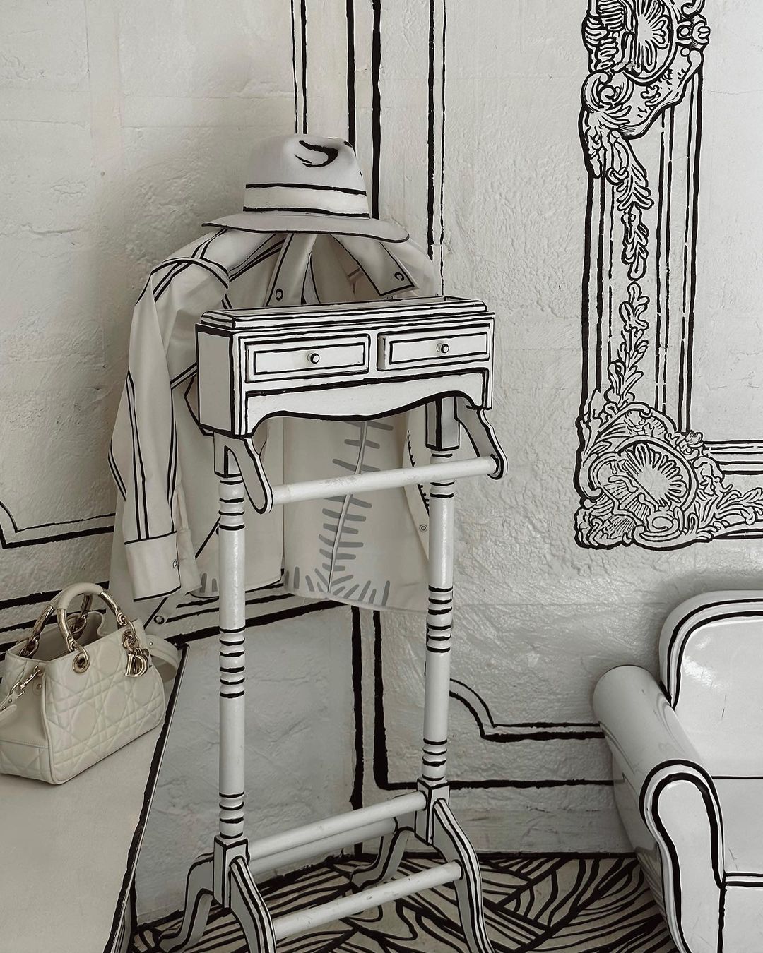 Monochrome cartoon-style interior: clothing rack with jacket and hat, white designer purse, sketched furniture in a decorated room.