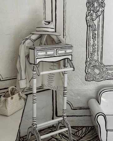 Monochrome cartoon-style interior: clothing rack with jacket and hat, white designer purse, sketched furniture in a decorated room.