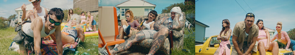 Group of people socializing outdoors on a sunny day in front of houses and a yellow car, casually dressed with tattoos and retro props.