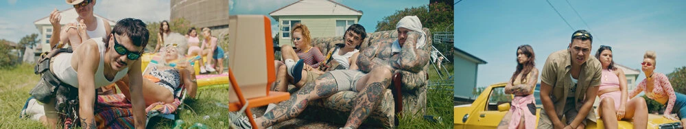 Group of people socializing outdoors on a sunny day in front of houses and a yellow car, casually dressed with tattoos and retro props.