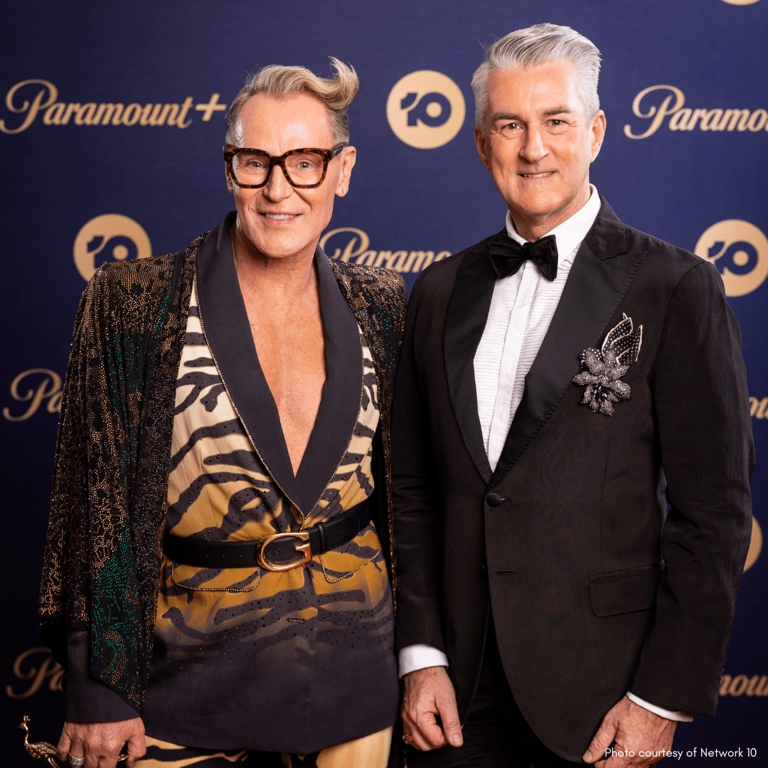 Two adult males in formal attire stand in front of a Paramount+ backdrop, one in a tuxedo and the other in a tiger-print jacket.