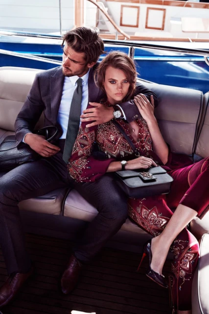 Attractive couple on a luxury yacht, man in suit and woman in ornate dress, showcase fashion and elegance against a water background.