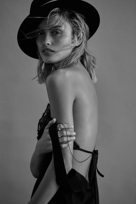 Black and white portrait of a woman with a hat looking at the camera, wearing a dress with thin straps, and shot in a photo studio.