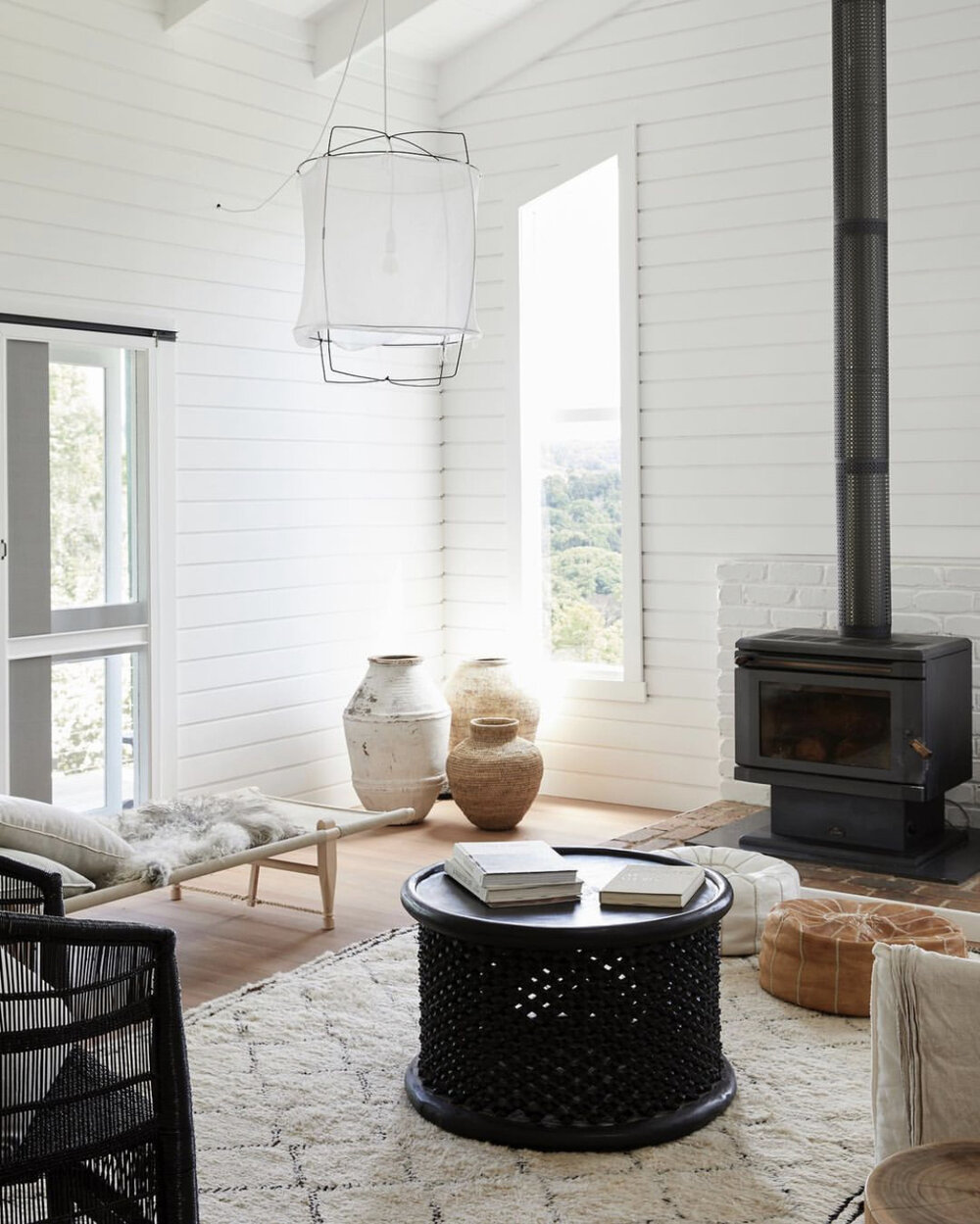 Living room interior with white plank walls, a black coffee table with books, vases, and a fireplace with a black stove.