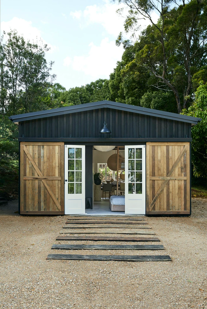 Exterior view of a dark wooden shed with large sliding barn doors and white French doors opening to an interior space.