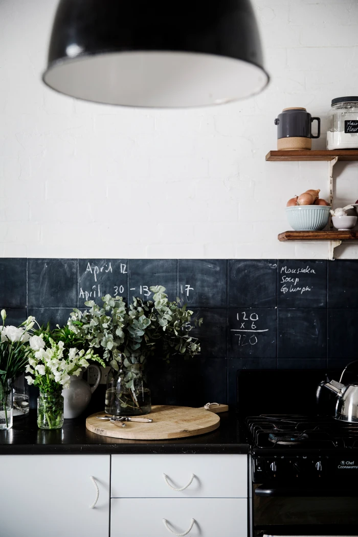 Interior kitchen styling featuring wooden cutting board, fresh flowers, and chalkboard tile backsplash by Natalie Walton