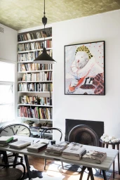 Interior view of a living room styled by Natalie Walton with a long wooden table covered in stacked books, built-in bookshelves, and art.