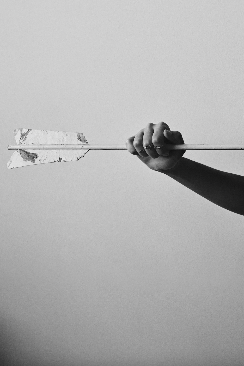 Monochrome image of a hand holding an arrow against a plain background, artistic in its simplicity and high contrast.