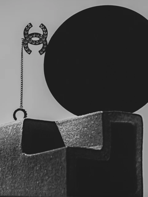 Black and white still life features a fashion brooch, black circular object and a textured block, artfully arranged.