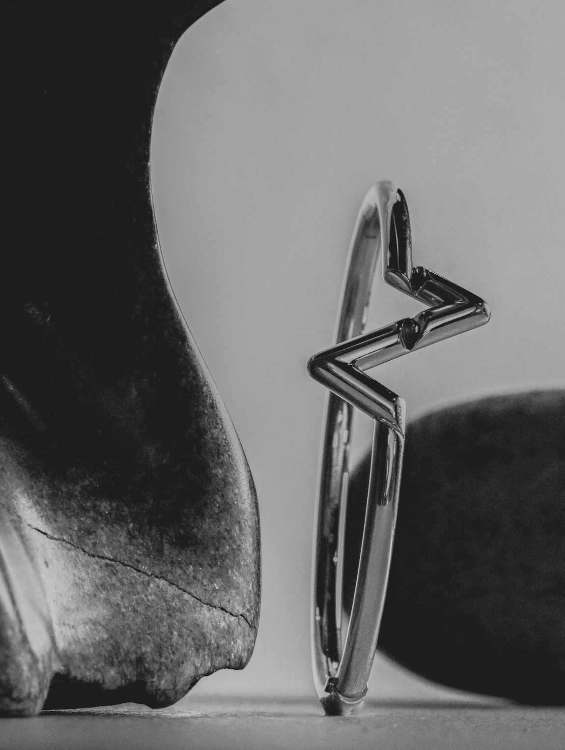 Close-up studio shot of a metallic silver bangle with a star shape next to rocks in a monochromatic colour palette.