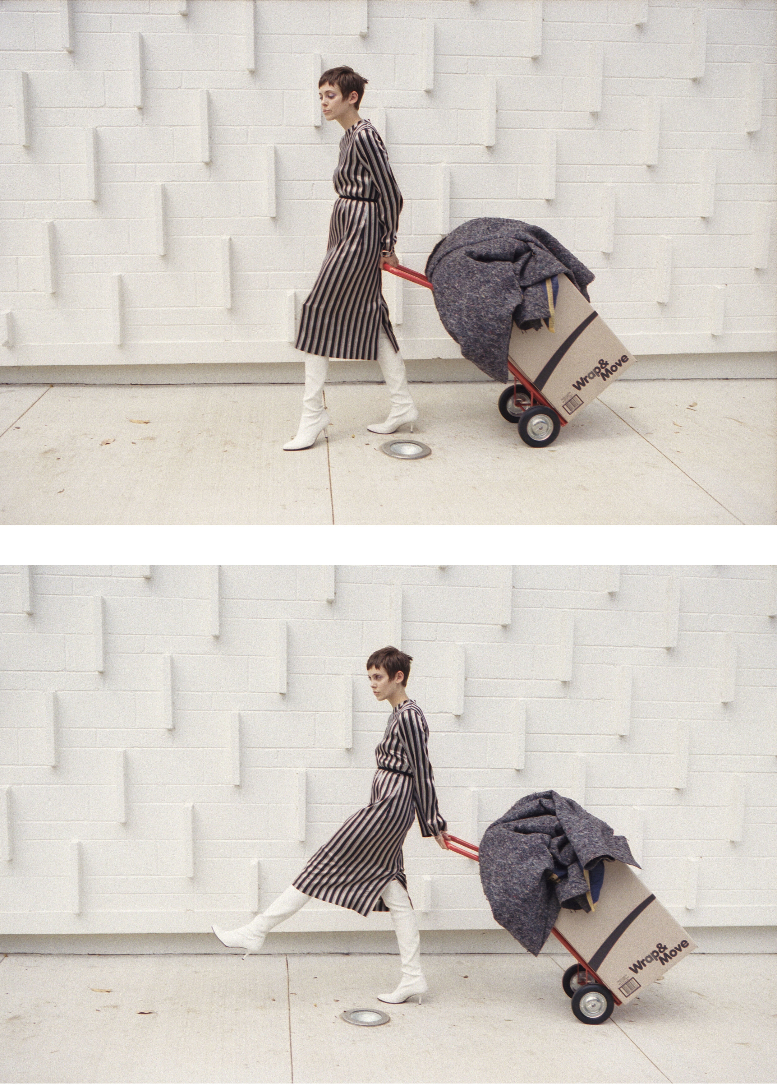 Woman in a striped dress and white boots walking with a hand truck and a box in front of a textured white wall.