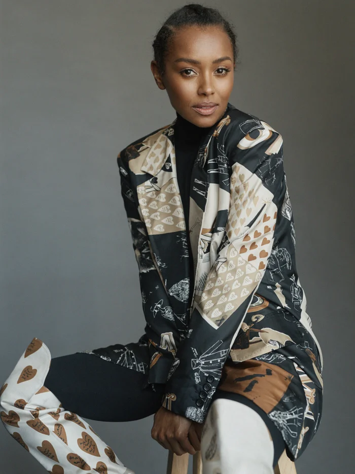 Portrait of a black woman wearing a patterned blazer and matching thigh-high boots, styled by Natalie Petrevski.