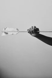 Close-up monochrome image of a hand holding an arrow horizontally against a plain light wall.