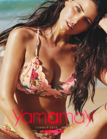 Brunette woman poses in floral bikini top on a beach, with ocean and sky visible in the background. Fashion, beauty, and summer vibe.