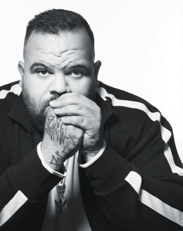 Monochrome portrait of a man with hand tattoos wearing a striped jacket against a white background