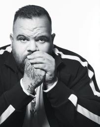 Monochrome portrait of a man with hand tattoos wearing a striped jacket against a white background