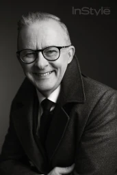 Monochrome portrait of Anthony Albanese wearing round eyeglasses and a dark wool coat with a turned-up collar