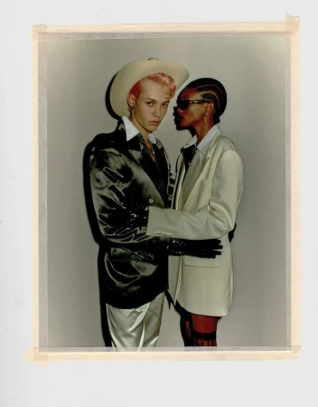 Polaroid photograph featuring two models posing together against a plain grey backdrop, styled by Madison Voloshin.