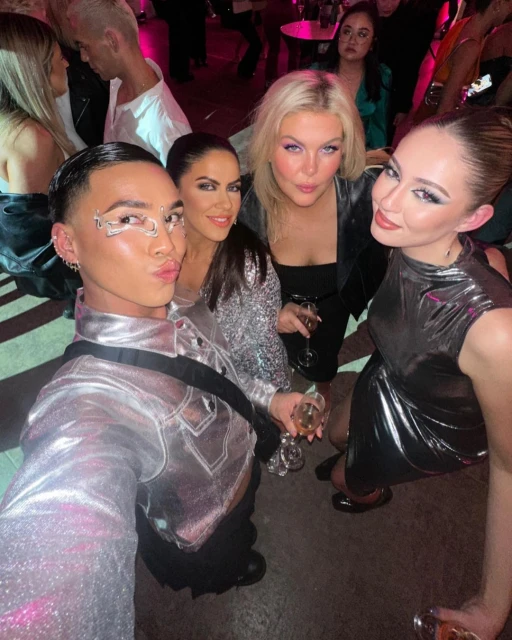 Group of five women posing for a selfie indoors, wearing stylish clothing and holding champagne glasses, capturing a fun moment with friends.