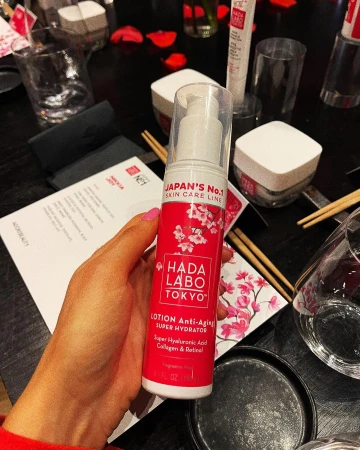 Close-up shot of Hada Labo Tokyo lotion in a woman's hand, skincare line, with dining table, plates, glasses, and chopsticks in view.
