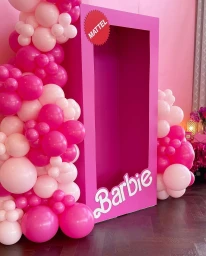 Giant pink Barbie toy box display framed by an elaborate balloon garland in shades of pink, white, and magenta.