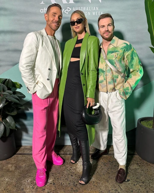 Three people pose together at Australian Fashion Week: two men in white and green shirts and a woman in a green leather coat.