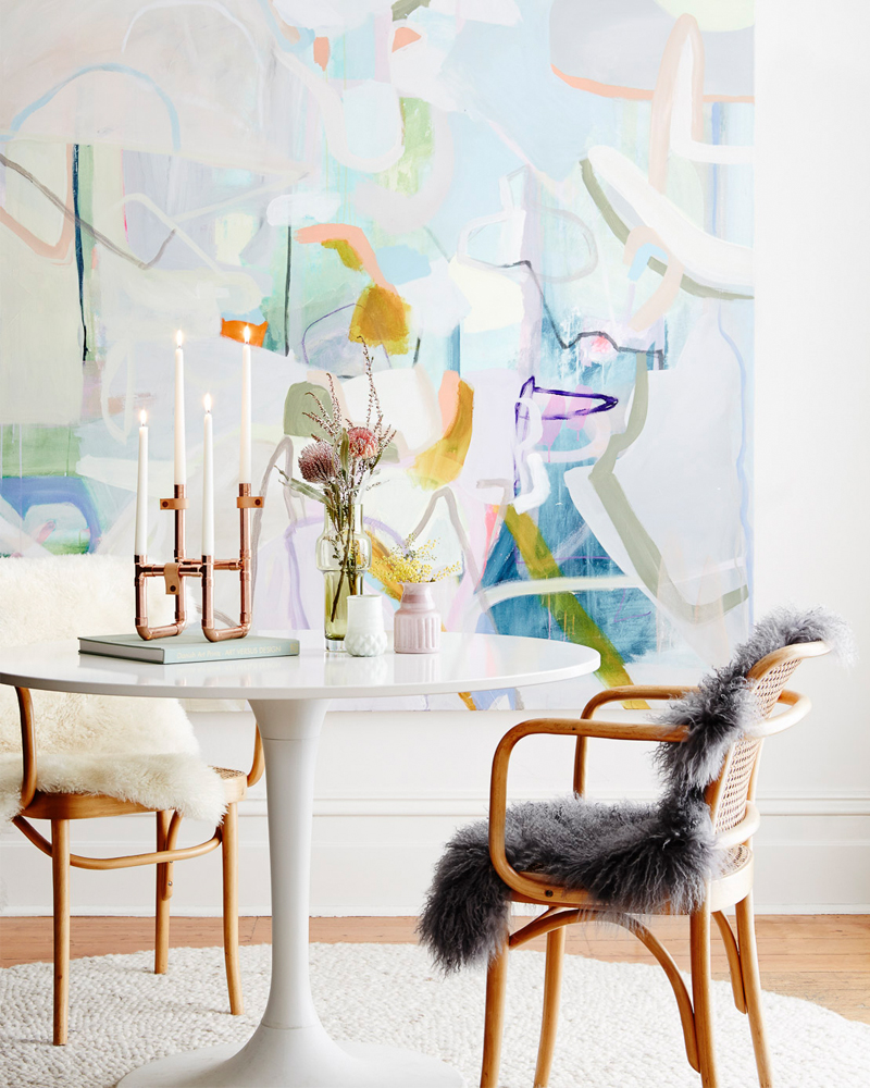 Interior view of a dining room featuring a round white table with a copper candle holder, flowers, and a light wood chair with a faux fur throw.
