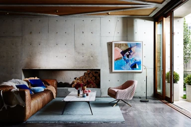 Modern living room featuring a concrete wall, brown leather sofa, pink armchair, and marble coffee table styled by Noel Coughlan.