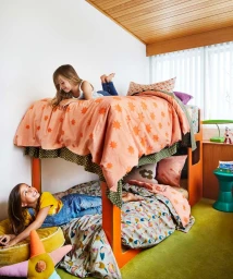 Two young girls playing in a brightly lit children bedroom with an orange wooden bunk bed and green carpet