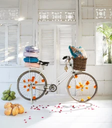 White vintage bicycle decorated with orange flower blossoms and stacked cushions against a white louvered wall