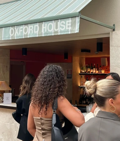 Patrons standing outside Oxford House venue, enjoying a drink at an outdoor bar with modern design and a striped awning.
