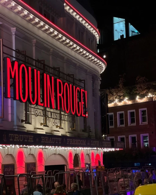 Exterior view of the Moulin Rouge theater at night with bright red neon signage and building details illuminated.