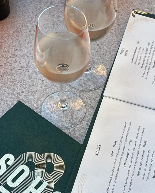 Two wine glasses filled with white wine sit on a table next to a menu at a restaurant, presenting a simple, elegant composition.