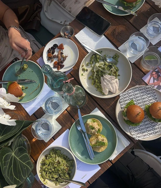 Overhead shot of a wooden table setting with various plates of food, drinks, and dining utensils. A smartphone sits on the table.
