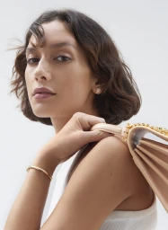 Close up portrait of a woman with short dark wavy hair holding a pale pink shoulder bag with a gold chain