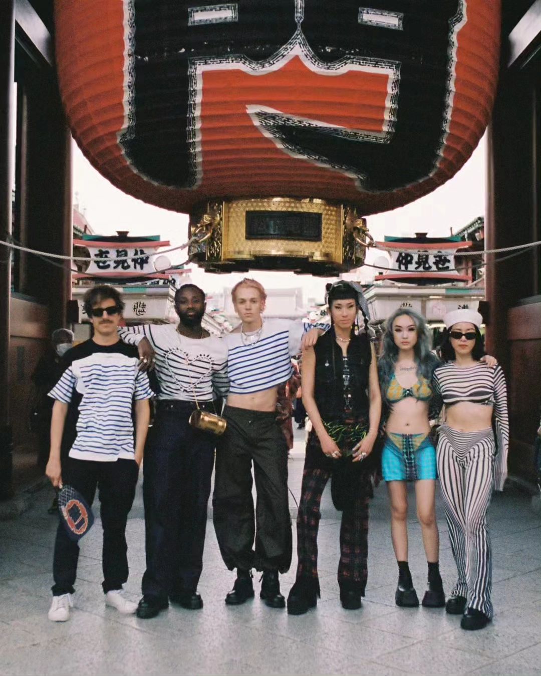 Group of six people in fashionable streetwear stand in front of the Senso-ji temple's Kaminarimon Gate in Tokyo, Japan.