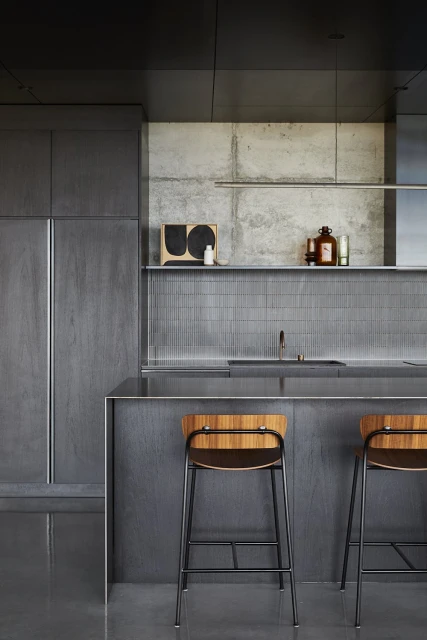 Minimalist kitchen design with grey cabinets, concrete walls, wood and metal bar stools, and natural light for a modern aesthetic.