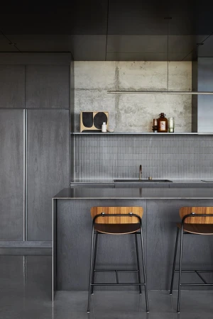 Minimalist kitchen design with grey cabinets, concrete walls, wood and metal bar stools, and natural light for a modern aesthetic.