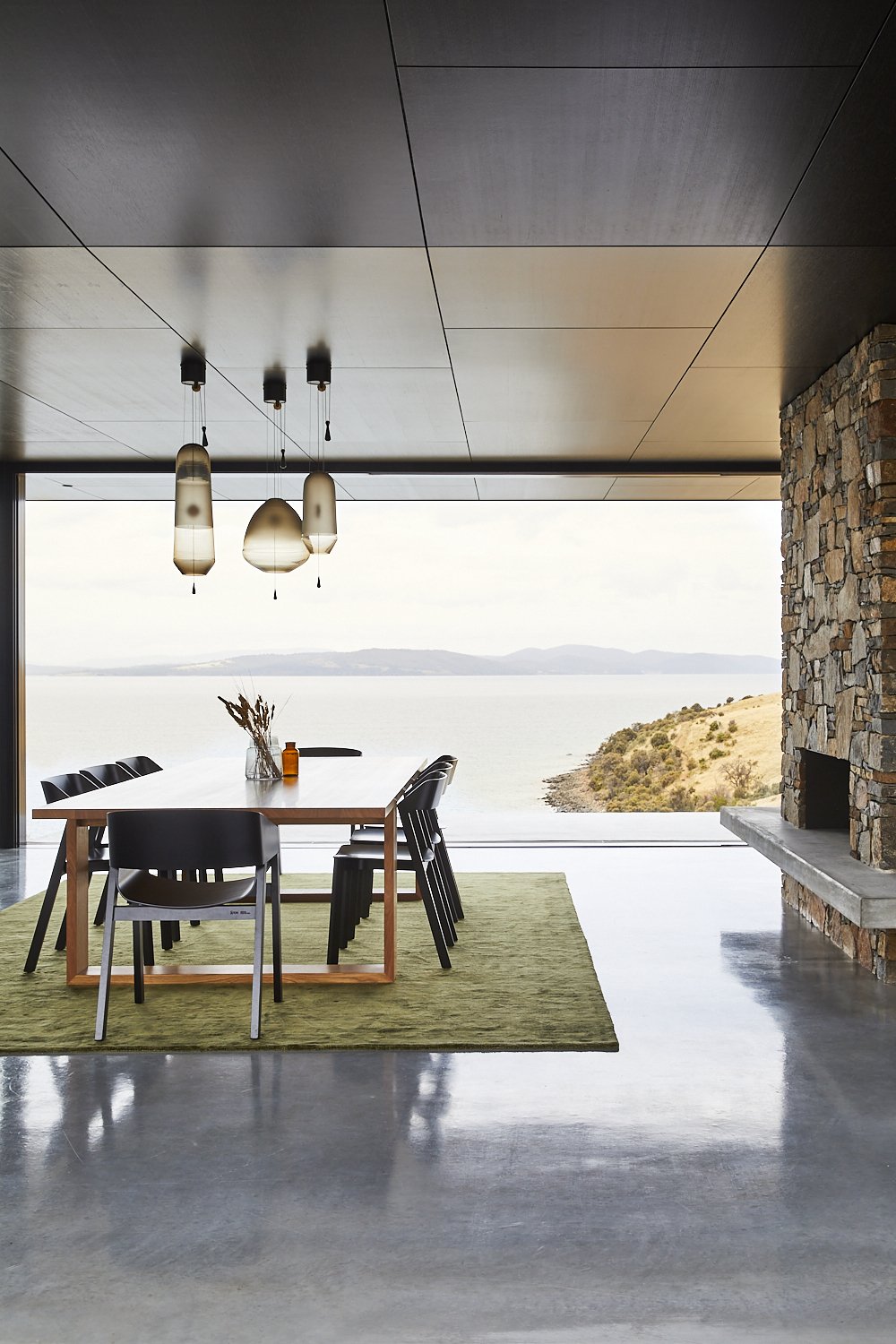 Dining room with a wooden table, chairs, and modern pendant lights, showcasing contemporary interior design and an ocean view.