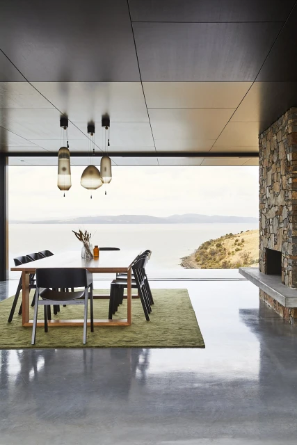 Dining room with a wooden table, chairs, and modern pendant lights, showcasing contemporary interior design and an ocean view.