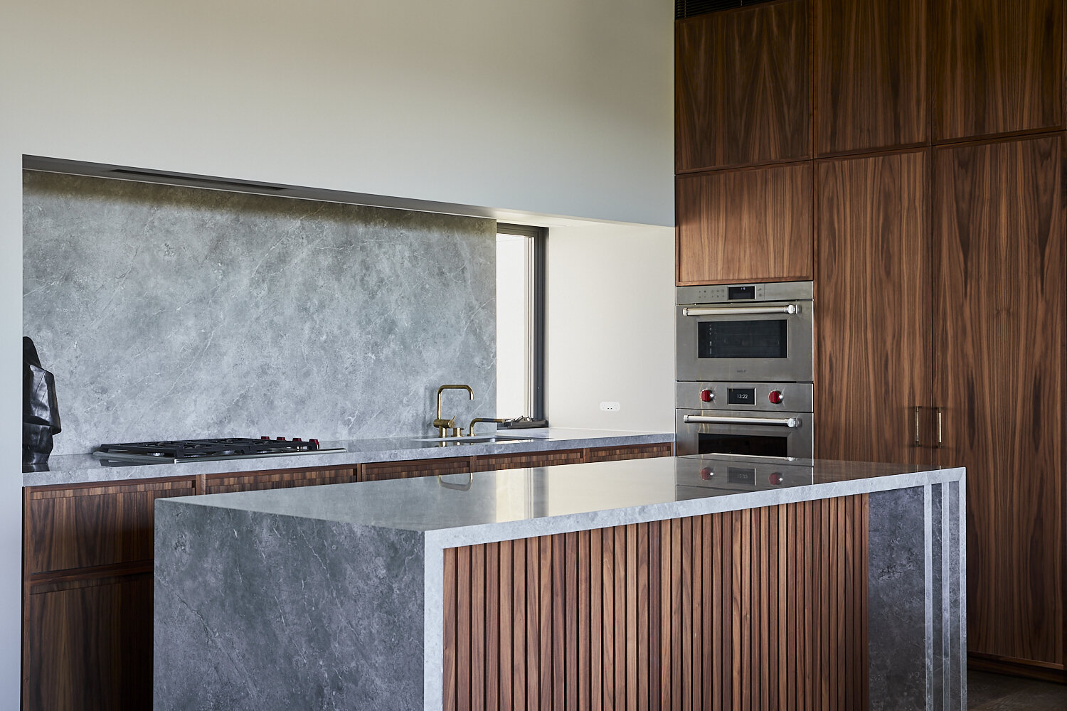 Modern kitchen interior with dark wood cabinetry, marble backsplash, and a central island featuring a marble countertop.