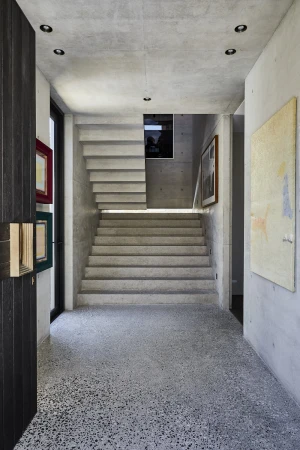 Modern interior hallway featuring exposed concrete walls, terrazzo flooring, and a floating concrete staircase.