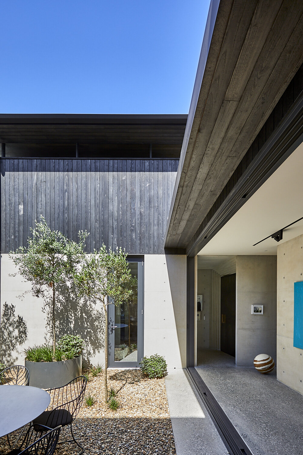 Exterior shot of a modern home with black wood siding, an open-air interior courtyard, a small tree, and gravel ground cover.