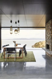 Contemporary dining room with wooden table, black chairs, and stone fireplace overlooking ocean view by Pablo Veigo