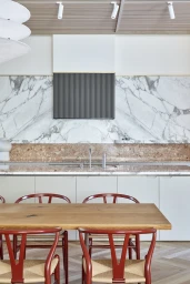 Modern kitchen interior featuring a marble backsplash, wooden dining table, and red chairs photographed by Pablo Veigo.