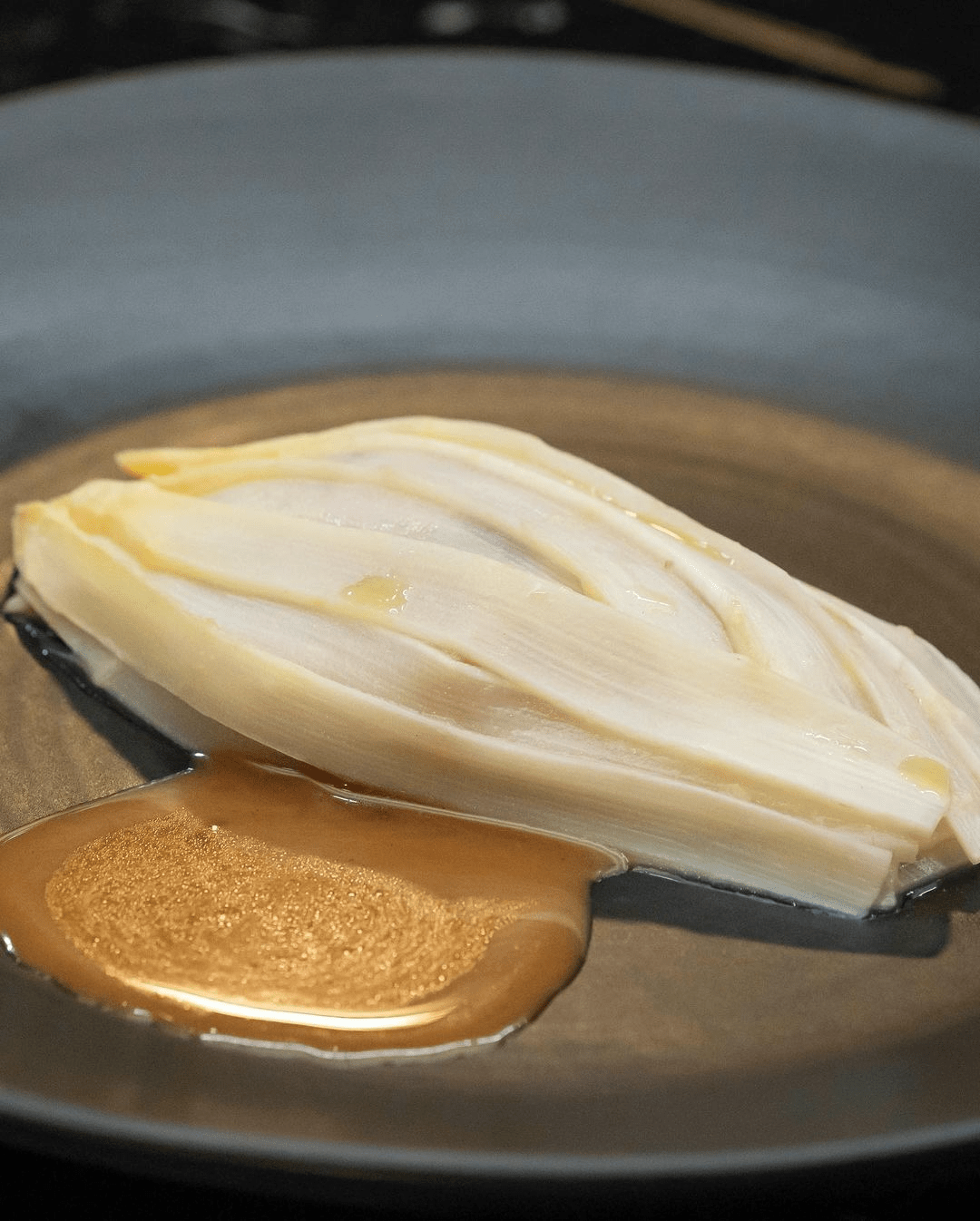 Close-up of braised endive with sauce on a gray plate showcases culinary presentation and simple food photography.